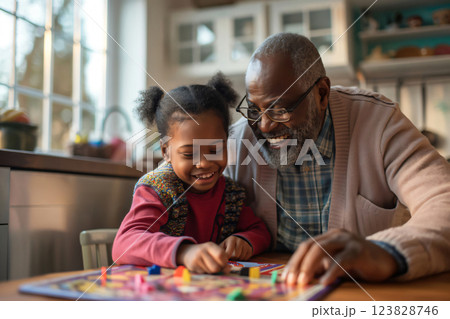 Grandfather and his granddaughter are spending quality time together, playing a board game at home. They are both smiling and having fun Grandfather and his granddaughter are spending quality time together, playing a board game at home. They are both smiling and having fun 123828746
