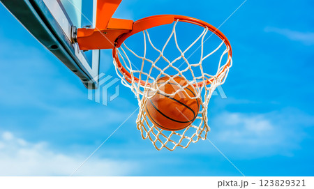 A basketball swishes through the net under a clear blue sky at the local court 123829321