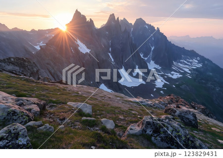 Beautiful sun rays piercing the horizon at sunrise, highlighting a rugged mountain landscape with snow patches and a clear sky 123829431