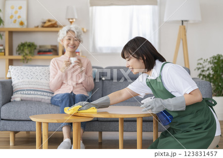 家事代行イメージ　ハウスクリーニングをする30代の女性とソファでくつろぐシニア女性 123831457