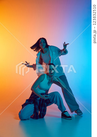 Two young female hip hop dancers i casual clothes energetically performing against gradient studio background in neon light Two young female hip hop dancers i casual clothes energetically performing against gradient studio background in neon light 123832510