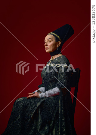 Elder noblewoman in renaissance dress sitting elegantly against deep red background, gazing forward with thoughtful expression. 123832579