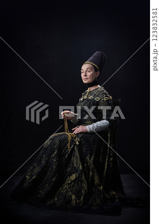 Elder noblewoman in renaissance dress holding golden necklace with cross, gazing forward with serene expression against dark background. Elder noblewoman in renaissance dress holding golden necklace with cross, gazing forward with serene expression against dark background. 123832581