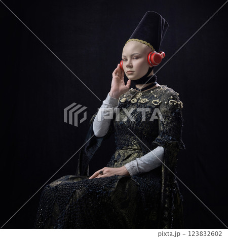 Young noblewoman in renaissance dress wearing modern red headphones, listening with calm expression against dark background. Young noblewoman in renaissance dress wearing modern red headphones, listening with calm expression against dark background. 123832602