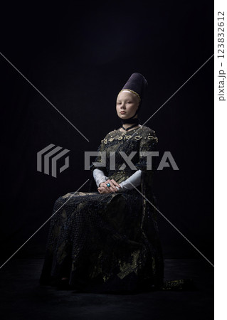 Portrait of young confident woman dressed renaissance style clothes, with calm expression looking at camera against dark vintage background. 123832612