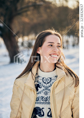 Cheerful young woman in beige winter coat and patterned sweater looks away with happiness on sunny day in park. Cheerful young woman in beige winter coat and patterned sweater looks away with happiness on sunny day in park. 123832637