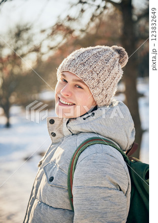Happy, smiling young man dressed cozy., warm winter clothes looking at camera, sharing his excitement, while he walking in snowy park on sunny winter day. Happy, smiling young man dressed cozy., warm winter clothes looking at camera, sharing his excitement, while he walking in snowy park on sunny winter day. 123832649