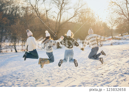 Smiling friends, men and women, jumping with excitement, fun and joy, tossing snow in air, celebrating winter outdoors. 123832658