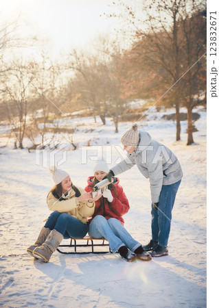 Group of friends sitting in snow, on sleds, sharing hot drinks, enjoying cozy winter moment together. Concept of winter, vacation Group of friends sitting in snow, on sleds, sharing hot drinks, enjoying cozy winter moment together. Concept of winter, vacation 123832671