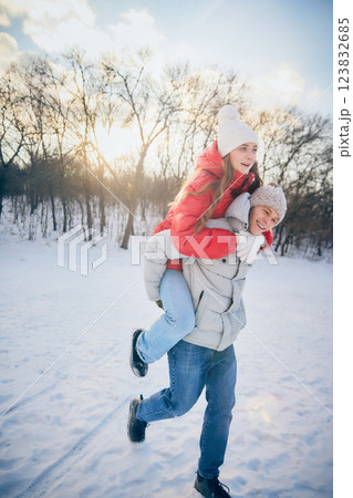 Young excited man carrying woman on back, both smiling and playing in winter wonderland, enjoying time together. 123832685