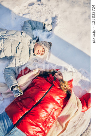 Man and woman resting on snowy ground, laughing together, feeling relaxed in peaceful winter landscape. Man and woman resting on snowy ground, laughing together, feeling relaxed in peaceful winter landscape. 123832724