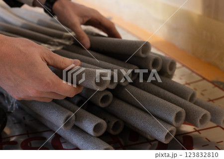 Man holding grey soft isolation for pipes of the water supply and heating system. Closeup, selective focus. 123832810