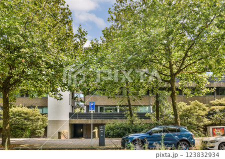 Contemporary architecture features a light-colored facade and green landscaping, set in an urban environment with a clear sky above. Contemporary architecture features a light-colored facade and green landscaping, set in an urban environment with a clear sky above. 123832934