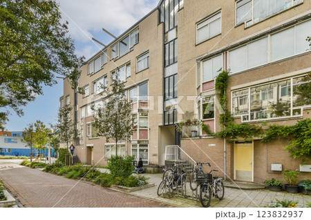An urban residential building featuring a contemporary design with greenery and bicycles parked outside. The sidewalk offers a well-maintained atmosphere. An urban residential building featuring a contemporary design with greenery and bicycles parked outside. The sidewalk offers a well-maintained atmosphere. 123832937