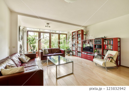 Spacious modern living room featuring large windows, hardwood flooring, and stylish furniture, creating a cozy and inviting atmosphere. 123832942