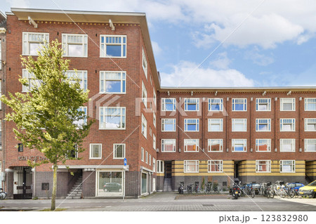 Showcasing contemporary urban buildings with red brick facades, large windows, and a tree, blending nature with architecture. 123832980