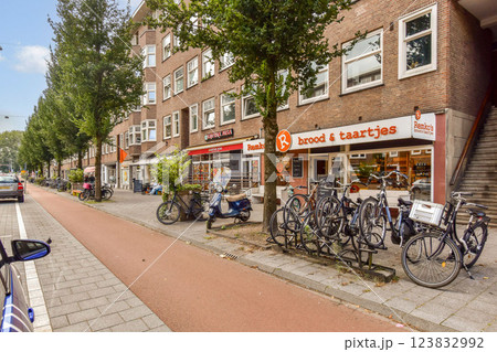 A vibrant city street displaying a mix of bicycles parked alongside local shops, framed by lush trees and a cozy urban atmosphere. A vibrant city street displaying a mix of bicycles parked alongside local shops, framed by lush trees and a cozy urban atmosphere. 123832992
