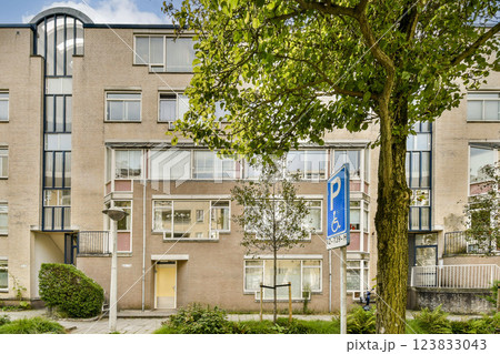 A contemporary residential building featuring large windows and a green exterior. The surrounding area includes trees and a parking sign, enhancing the urban environment. 123833043