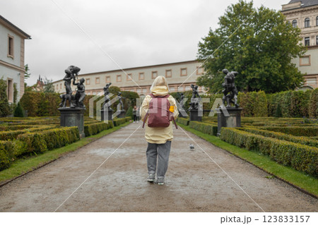 A female tourist walks around along a decorative alley decorated with many statues in a decorative park at Wallenstein Palace building in Prague in Czech Republic 123833157