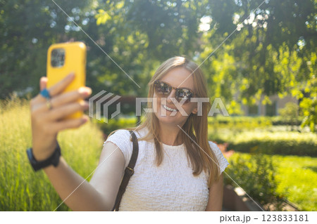 Cheerful smiling 30s lady taking selfie outdoors in city park, happy young female capturing self-portrait while enjoying walk and good day, resting outside 123833181