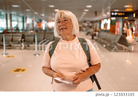 Happy blonde hair Elderly female tourist with a backpack with a passport while waiting for the passport check of the tourist at the airport Happy blonde hair Elderly female tourist with a backpack with a passport while waiting for the passport check of the tourist at the airport 123833185