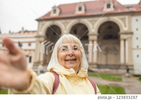 Happy 60s blonde elderly woman takes a selfie in Prague gardens at summer holiday in Europe. View of the Waldstein park in Prague-a famous tourist attraction. Prague, Czech Republic 123833287