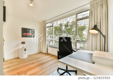 A contemporary workspace featuring a desk, chair, and large windows letting in natural light. Sleek design with minimalist decor enhances productivity. 123833503