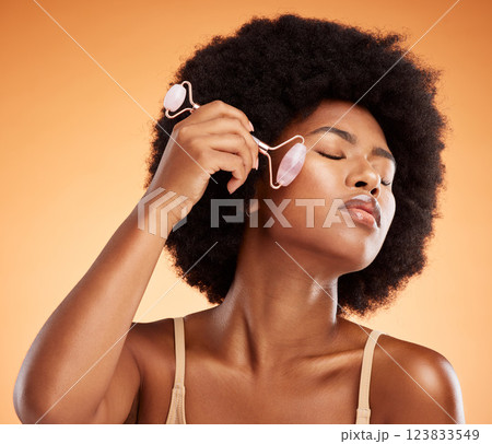 Beauty, afro and black woman with skincare derma roller for healthy and natural skin on face. Wellness and massage girl satisfied with rose quartz self care treatment with orange background. 123833549