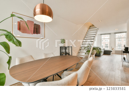 A contemporary interior featuring a wooden dining table, stylish chairs, and artistic wall decor, complemented by greenery for a fresh ambiance. 123833581