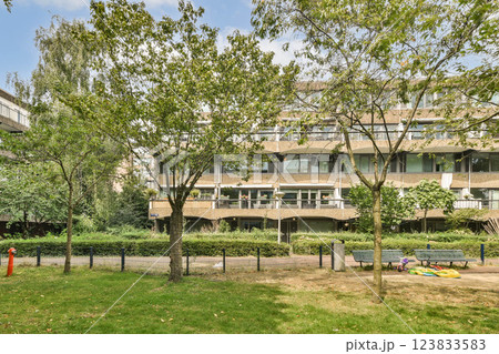 A serene urban park with lush greenery and modern architecture in the background, featuring benches and well-maintained pathways. 123833583