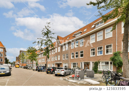 A picturesque street lined with classic brick buildings and lush trees. Cars are parked along the side, showcasing the serene neighborhood atmosphere. A picturesque street lined with classic brick buildings and lush trees. Cars are parked along the side, showcasing the serene neighborhood atmosphere. 123833595