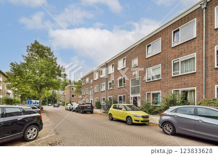 A serene view of a residential street featuring contemporary brick buildings, lush greenery, and parked cars under a clear sky. A serene view of a residential street featuring contemporary brick buildings, lush greenery, and parked cars under a clear sky. 123833628