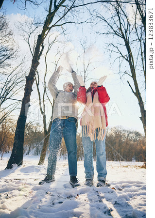 Smiling couple throwing snow in air, sharing joyful moment outdoors in snowy forest. View from low angle. 123833671