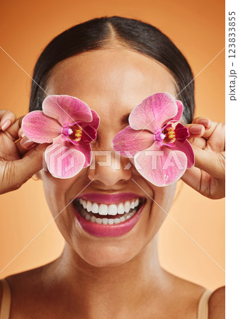 Orchid flower, creative art and beauty woman with makeup, cosmetic and smile on face against an orange background. Happy, floral and comic female model with plant for facial wellness and skincare Orchid flower, creative art and beauty woman with makeup, cosmetic and smile on face against an orange background. Happy, floral and comic female model with plant for facial wellness and skincare 123833855