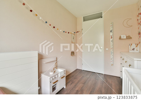 A beautifully designed nursery room featuring soft pastel colors, a stylish crib, playful decorations, and a warm wooden floor, creating a perfect space for a baby. 123833875