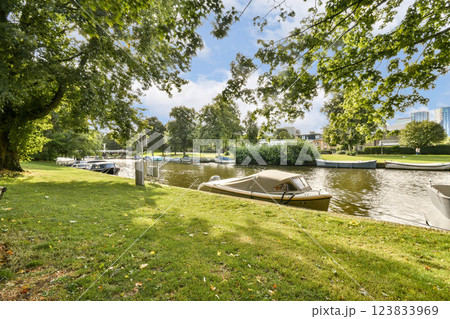 Lush green trees frame a tranquil waterway where boats are moored, creating a peaceful natural setting perfect for relaxation and reflection. 123833969