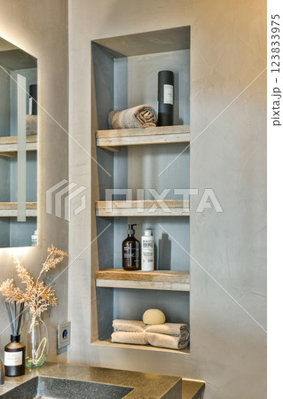 Aesthetic display of towels and toiletries on wooden shelves in a minimalist bathroom setting, complemented by natural decor elements. 123833975