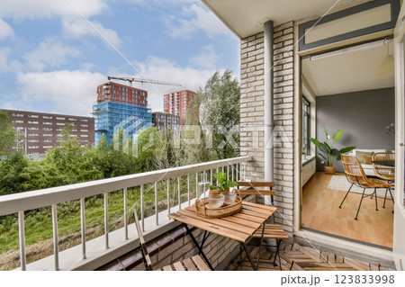 A stylish balcony featuring outdoor furniture, overlooking a mix of modern buildings and lush greenery under a clear sky. Perfect for relaxation and city living. A stylish balcony featuring outdoor furniture, overlooking a mix of modern buildings and lush greenery under a clear sky. Perfect for relaxation and city living. 123833998