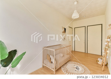 A bright and airy nursery featuring a wooden crib, soft round rug, and potted plants, ideal for a welcoming and peaceful environment for a baby. 123834012