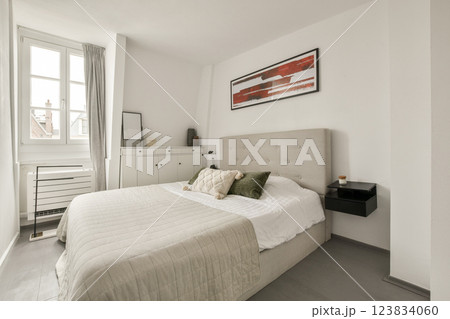 A sleek and minimalistic bedroom featuring neutral colors, a comfortable bed, and stylish decor. The design emphasizes simplicity and functionality in a cozy environment. 123834060