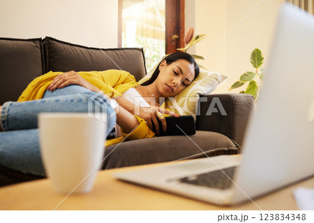 Tired woman, phone and relax for work break at home lying on living room sofa with technology. Female freelancer overworked, burnout and relaxing on a couch texting or streaming on mobile smartphone 123834348