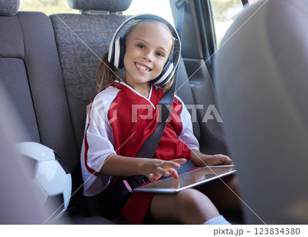 Soccer, car and girl with tablet for music traveling to football practice, exercise and childrens fitness workout. Smile, sports and happy kid in headphones enjoys drive trip to training on a weekend 123834380