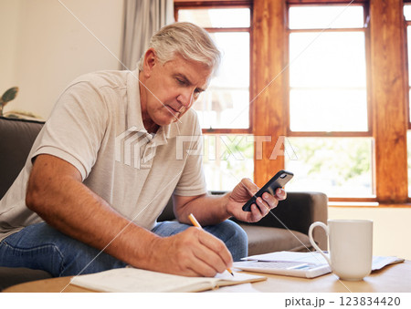 Smartphone, budget planning and senior man in living room for retirement research, website investment information or asset management. Elderly person writing notes, using phone online finance banking 123834420