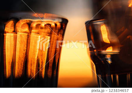 Closeup of wine glass, faceted tumbler, goblet, shot glass for drinks illuminated by orange light.  123834657