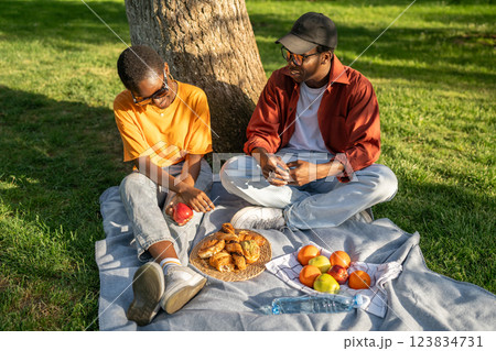 Young black couple sit on picnic blanket, eat and chat in park. Relaxed date in nature, city break Young black couple sit on picnic blanket, eat and chat in park. Relaxed date in nature, city break 123834731