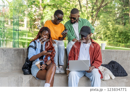 Group of interracial friends on bench work on laptops, phones. Digital native students exploring Net Group of interracial friends on bench work on laptops, phones. Digital native students exploring Net 123834771