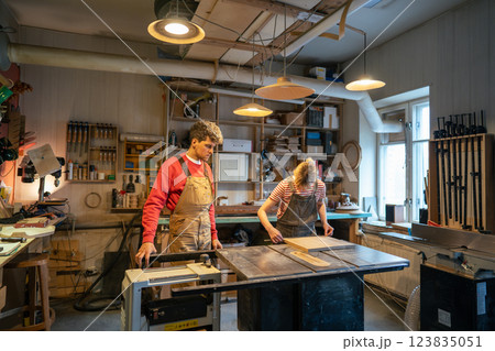 Carpenter man supervising novice woman working on circular saw table in woodworking workshop 123835051