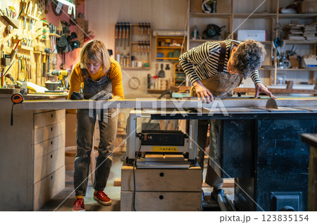 Carpentry colleagues handle circular saw station, measure wood beam with precision. Family business 123835154