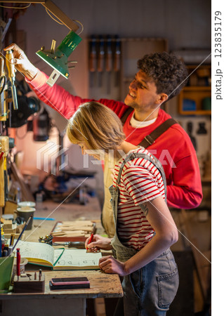 Smiling woodworker collaborate with assistant in carpentry workshop. Woman sketches furniture design 123835179