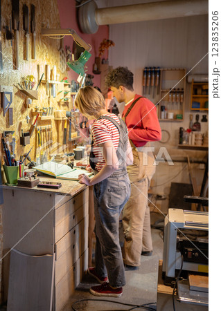 Busy carpenters track client orders for wood items. Woman record transaction, man arrange tools 123835206